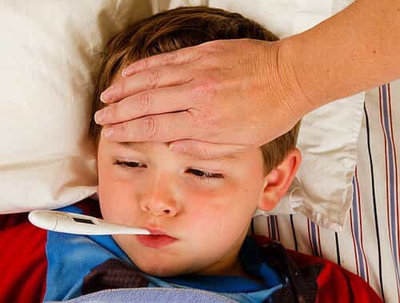Sick child in bed with a thermometer in his mouth and parent feeling his forehead